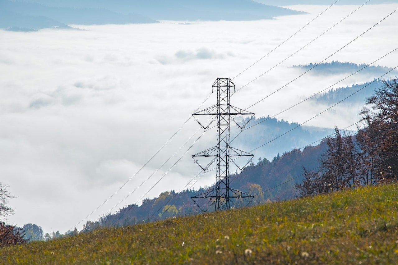 Electricity tower on green mountain with sky and clouds in background.